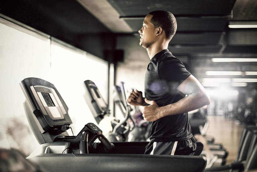 Healthy young man in gym running on treadmill.