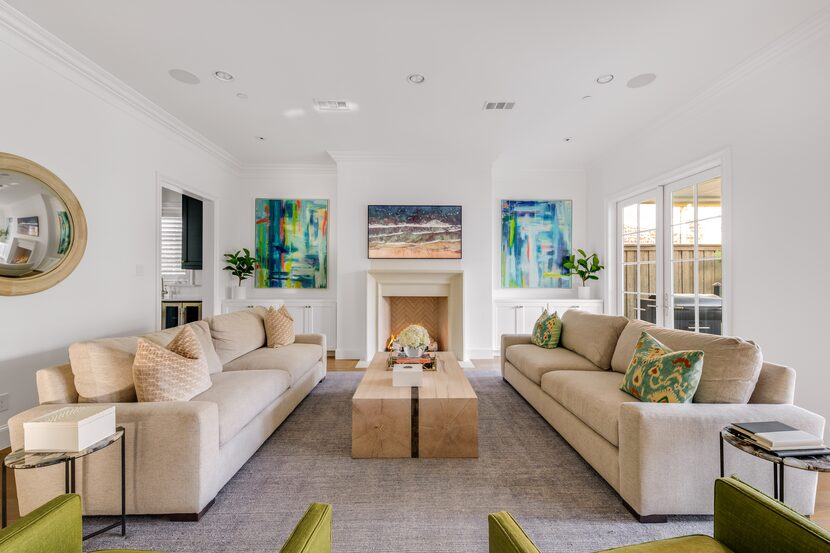 A living room with white walls and taupe couches also has a white fireplace.