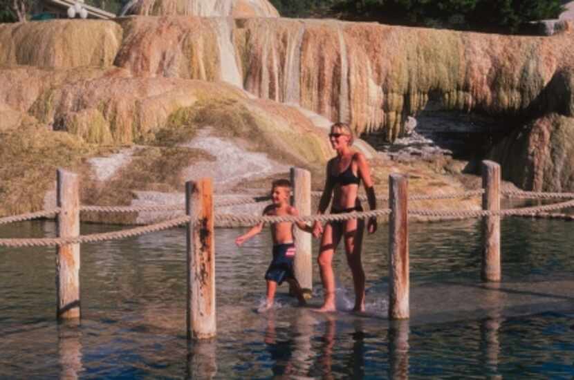 Bathers appear to walk on water using a submerged boardwalk to cross a large hot springs...