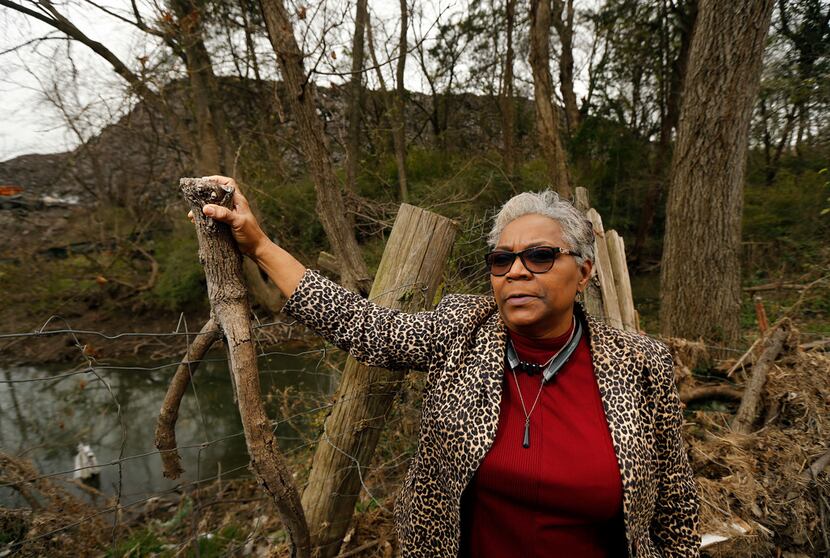 Homeowner Marsha Jackson stands alongside the flood-damaged fencing bordering a large hill...