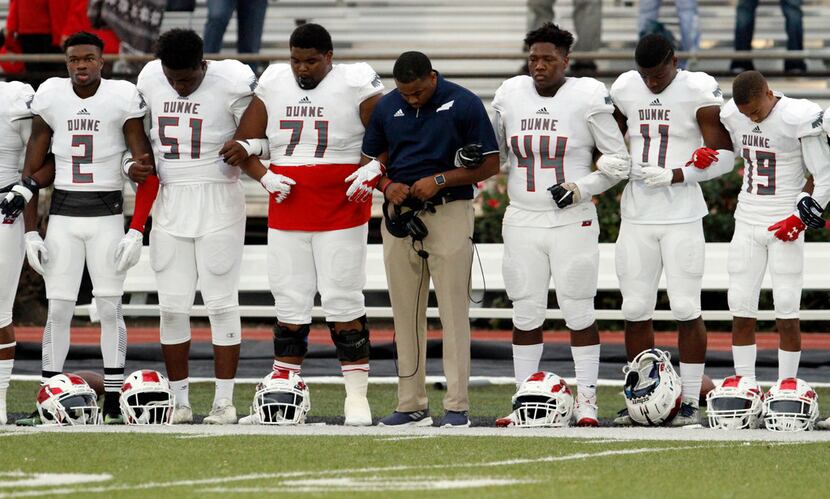 Bishop Dunne players lock arms with each other and a coach during the National Anthem before...