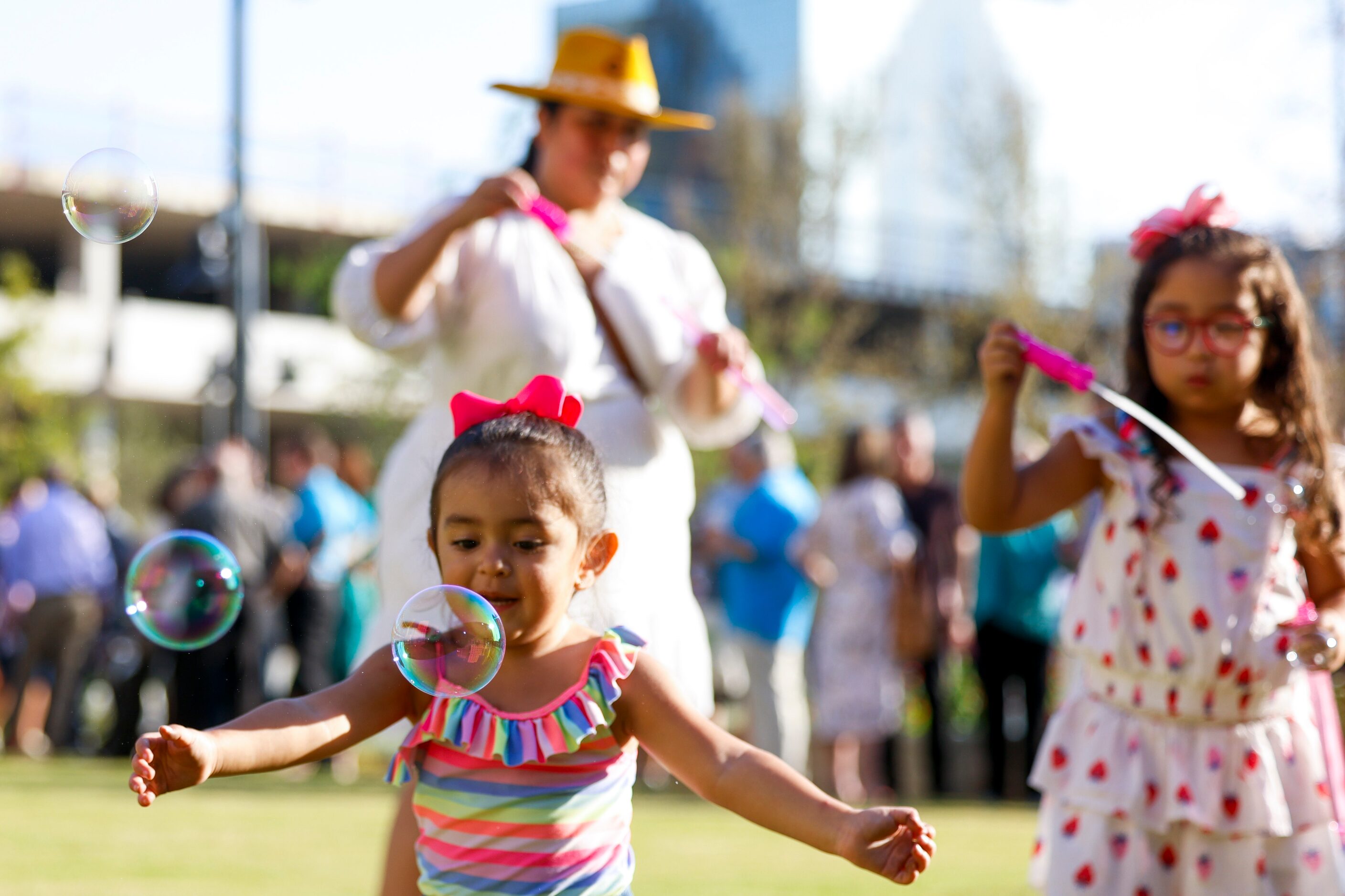 Noelle Huerta, 2, (front), plays on the open lawn with the soap bubbles from Monica Moreno...