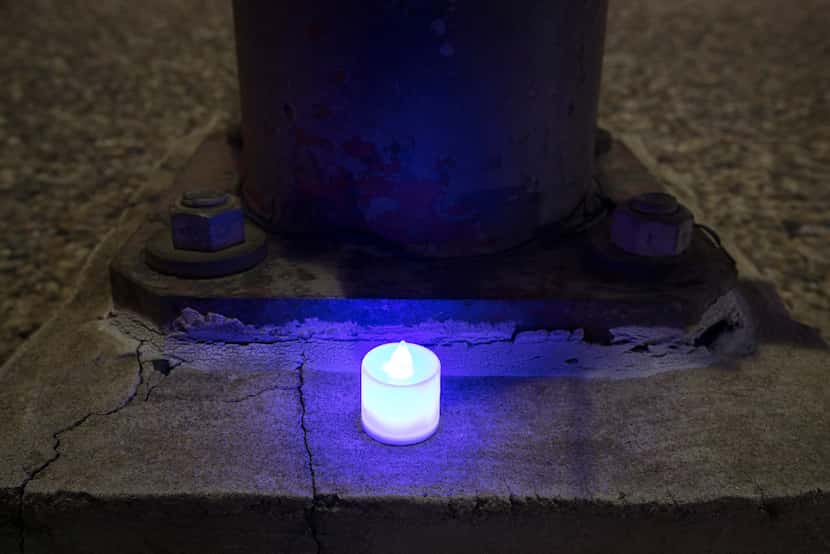 At 9:43 p.m., on a quiet sidewalk, a single blue electric candle glows next to a light pole...