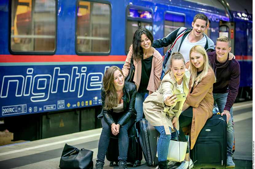Foto de cinco jóvenes con maletas enfrente de un tren.
