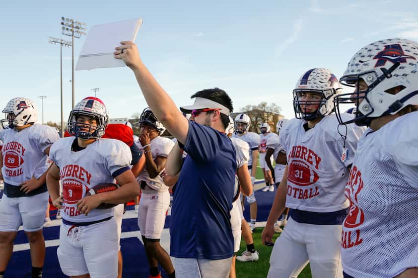 Defensive tackles coach Kye Ranton holds up a play during a football practice at Aubrey High...