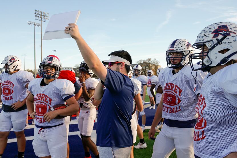 Defensive tackles coach Kye Ranton holds up a play during a football practice at Aubrey High...