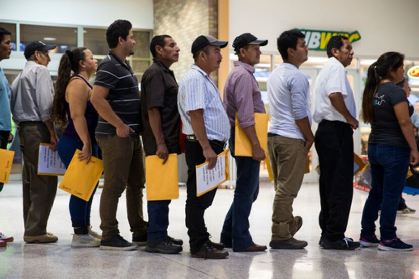 Un grupo de inmigrantes hacen fila para tomar un autobús en McAllen.