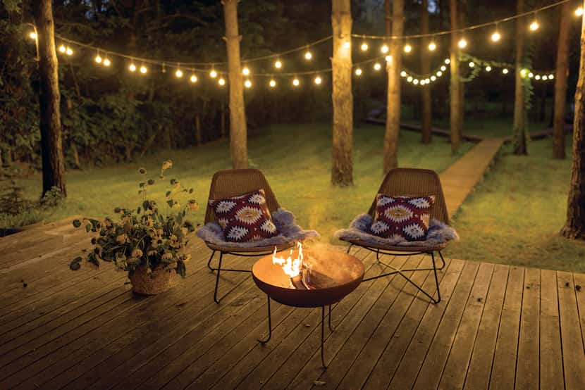 Two chairs sit next to a fireplace and string lights hang overhead.