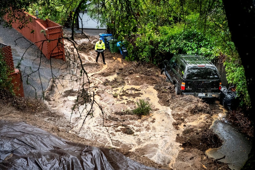 Permit Sonoma Director Tennis Wick crosses a mudslide to inspect a home as heavy rains fall...