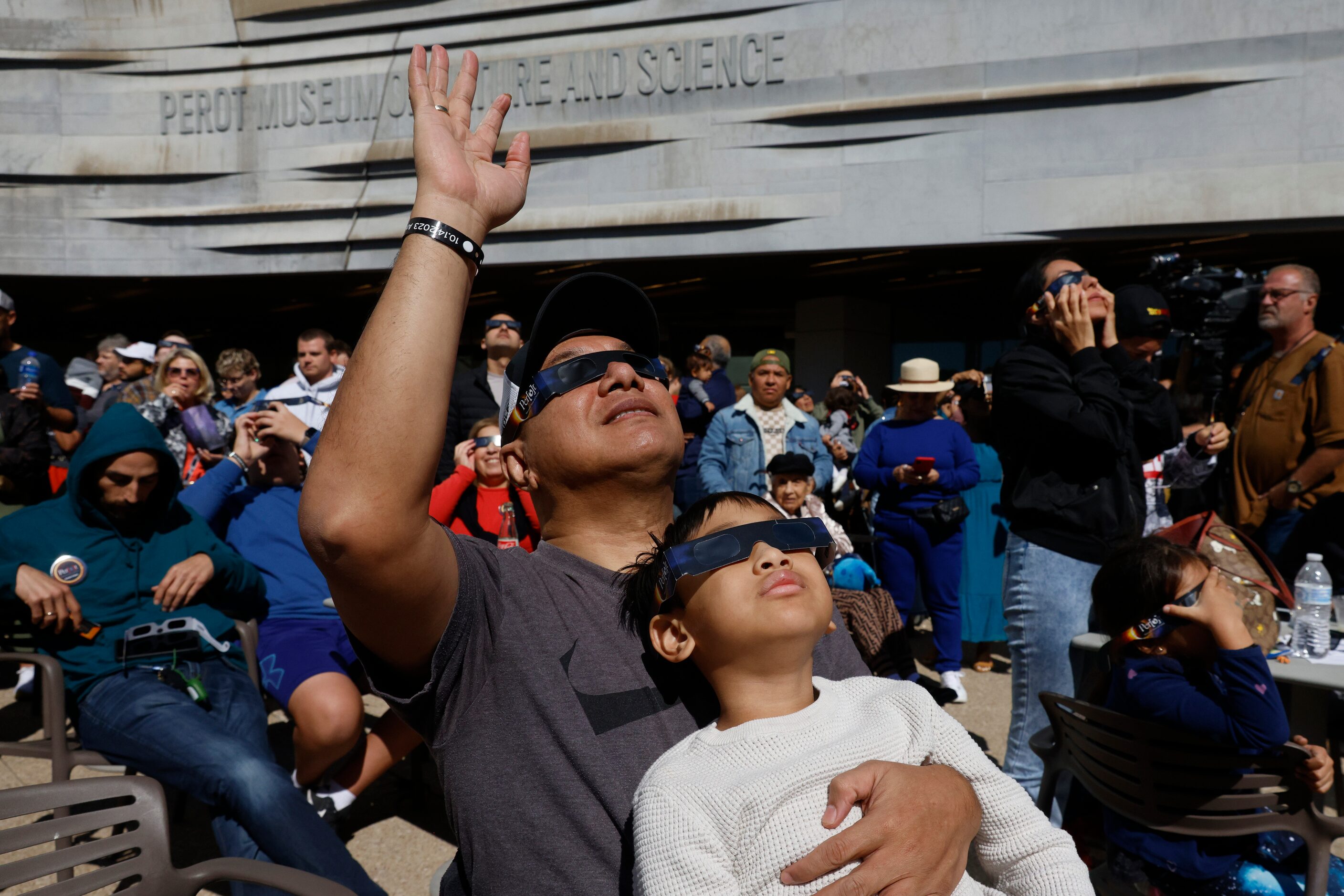 Juniper Panjaitan cheers while carrying his son Ferrel, 6, as he watches the peak of annular...