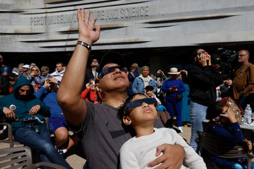Juniper Panjaitan cheers while holding his son Ferrel, 6, as they watch the peak of annular...