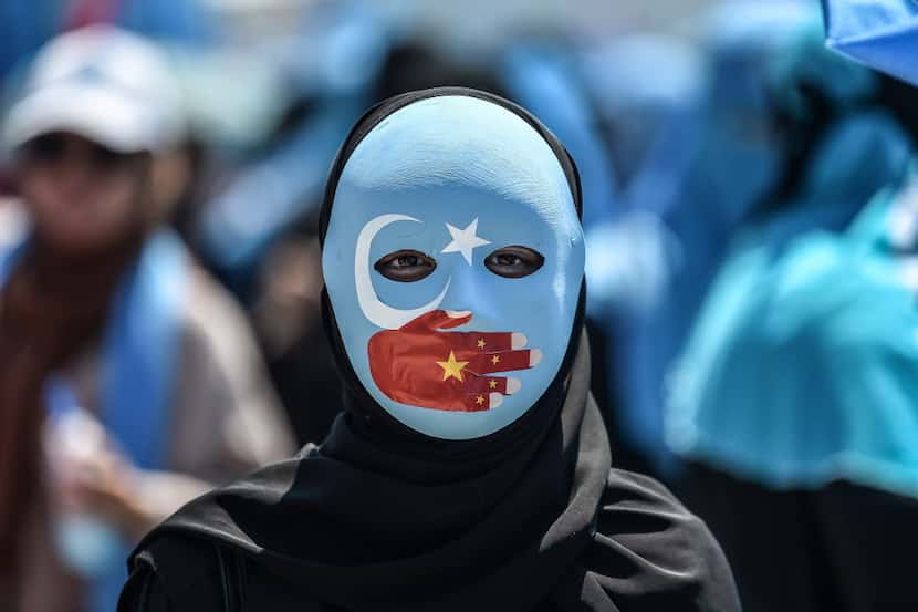 A demonstrator wearing a mask painted with the colors of the flag of East Turkestan and a...