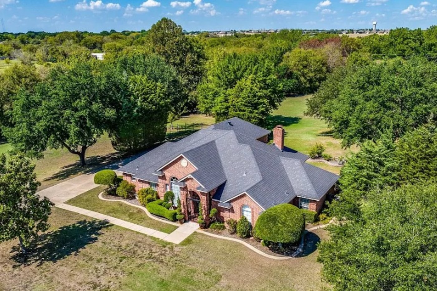 SIngle-story brick home surrounded by expansive green space and mature trees.