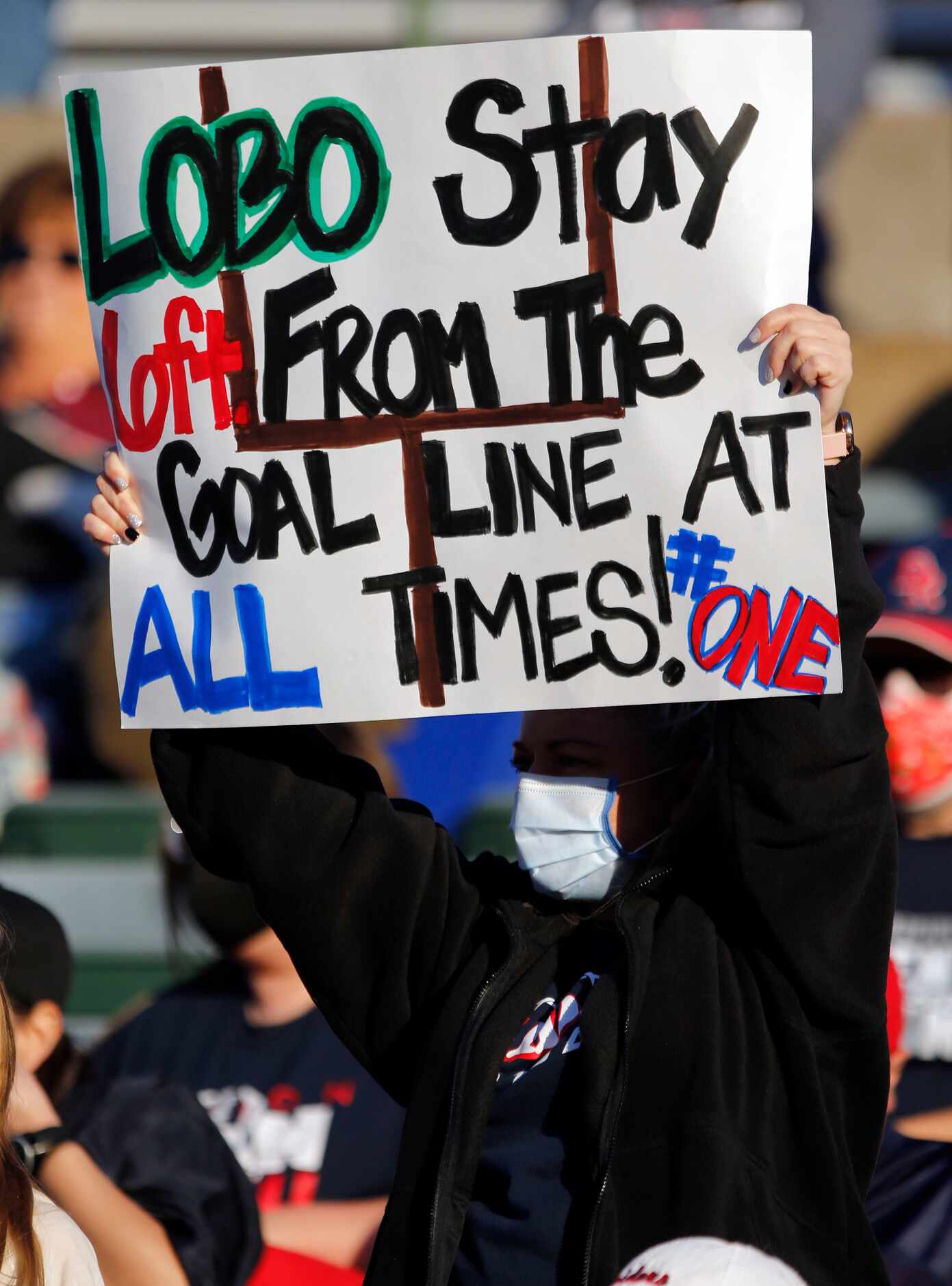 A Denton Ryan fan holds a social distancing sign that reads, “Lobo Stay 6ft from the Goal...