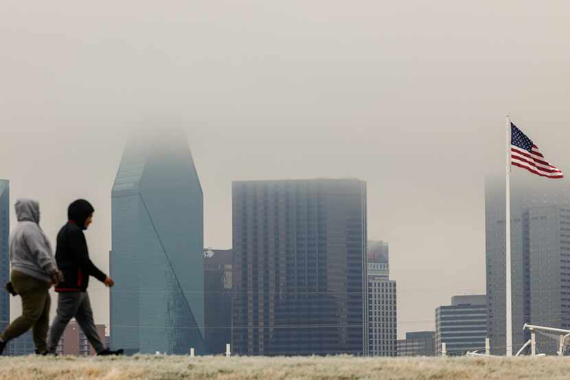People walk around Trinity Skyline trail as drizzly clouds cover part of downtown Dallas...