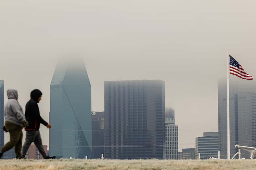 People walk around Trinity Skyline trail as drizzly clouds cover part of downtown Dallas...