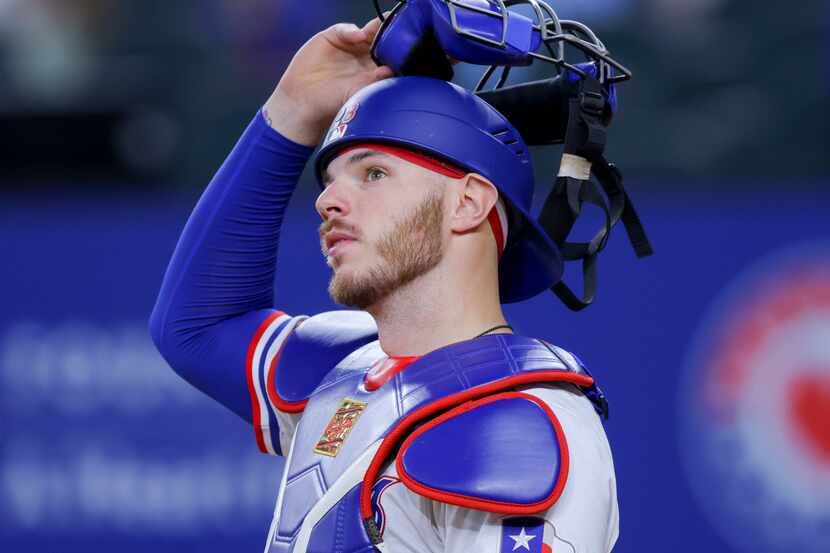 Texas Rangers catcher Jonah Heim readies his gear between innings of a baseball game against...