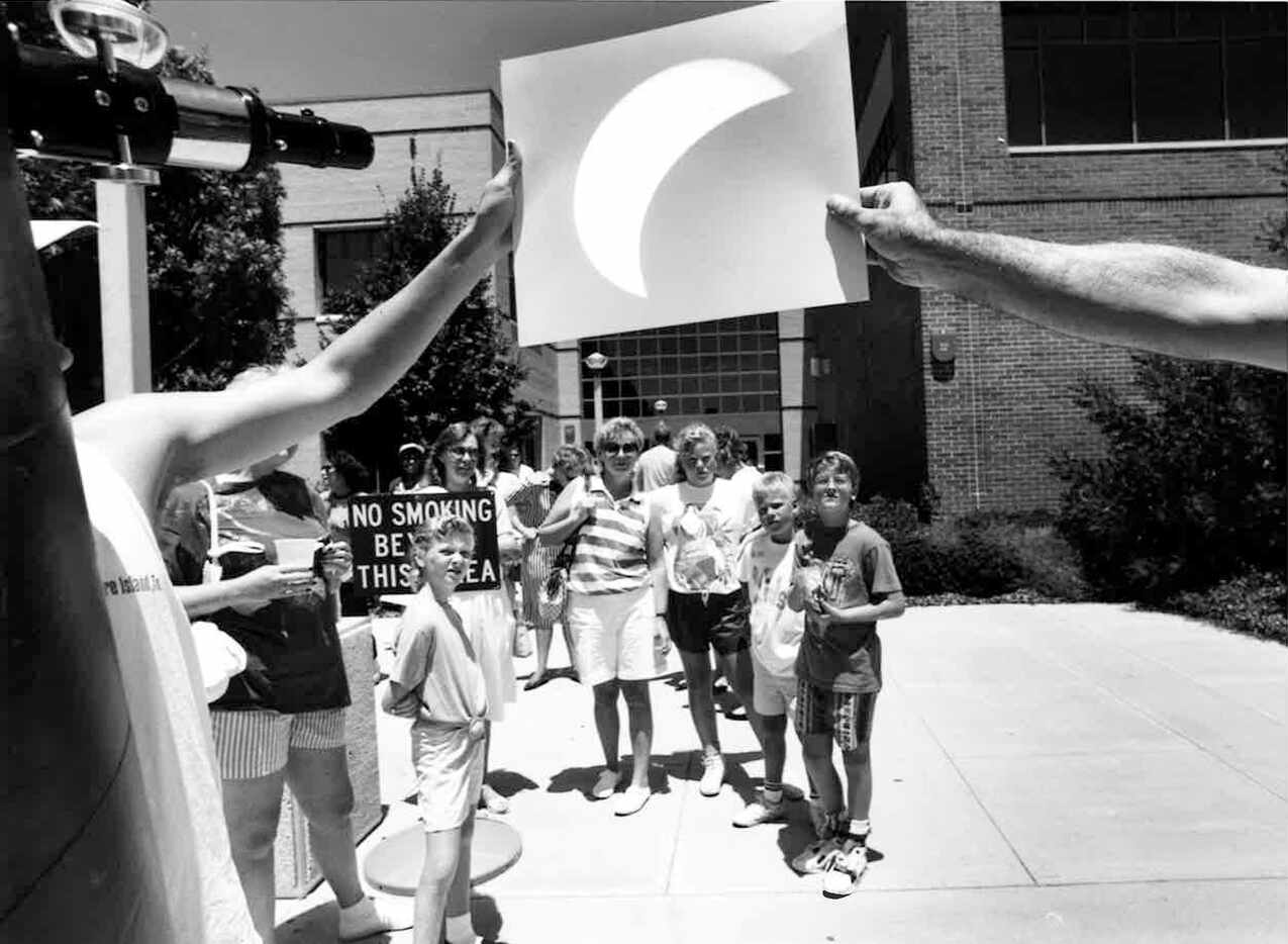 Mike Morrow and Matthew Coulter hold up a piece of paper to view the eclipse at the Collin...