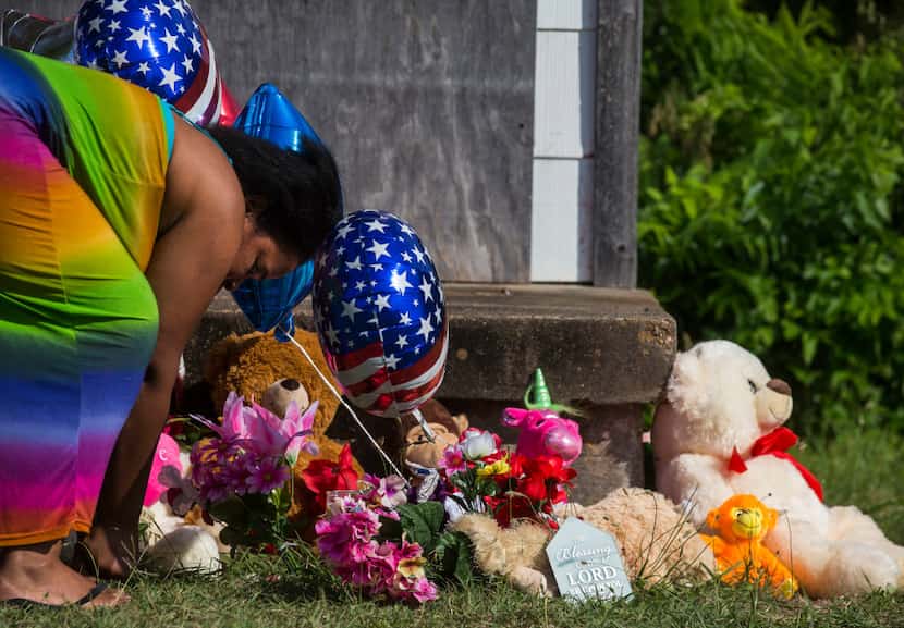 Adrian Moseley, of Dallas, plants a flower at a memorial as balloons and flowers wave in the...