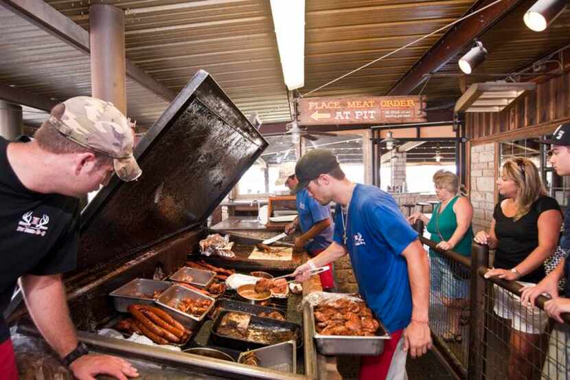 Pit worker Keith Baker, left, looks in on the offerings at Hard Eight Pit-Bar-B-Q in...