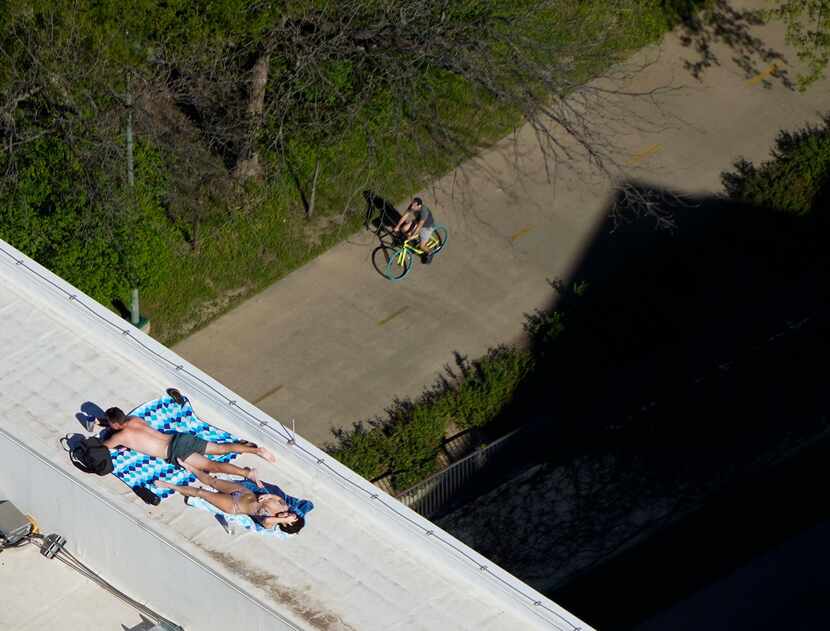 A couple sunbathes on the roof of the The Katy in Victory Park Apartments as a man rides by...
