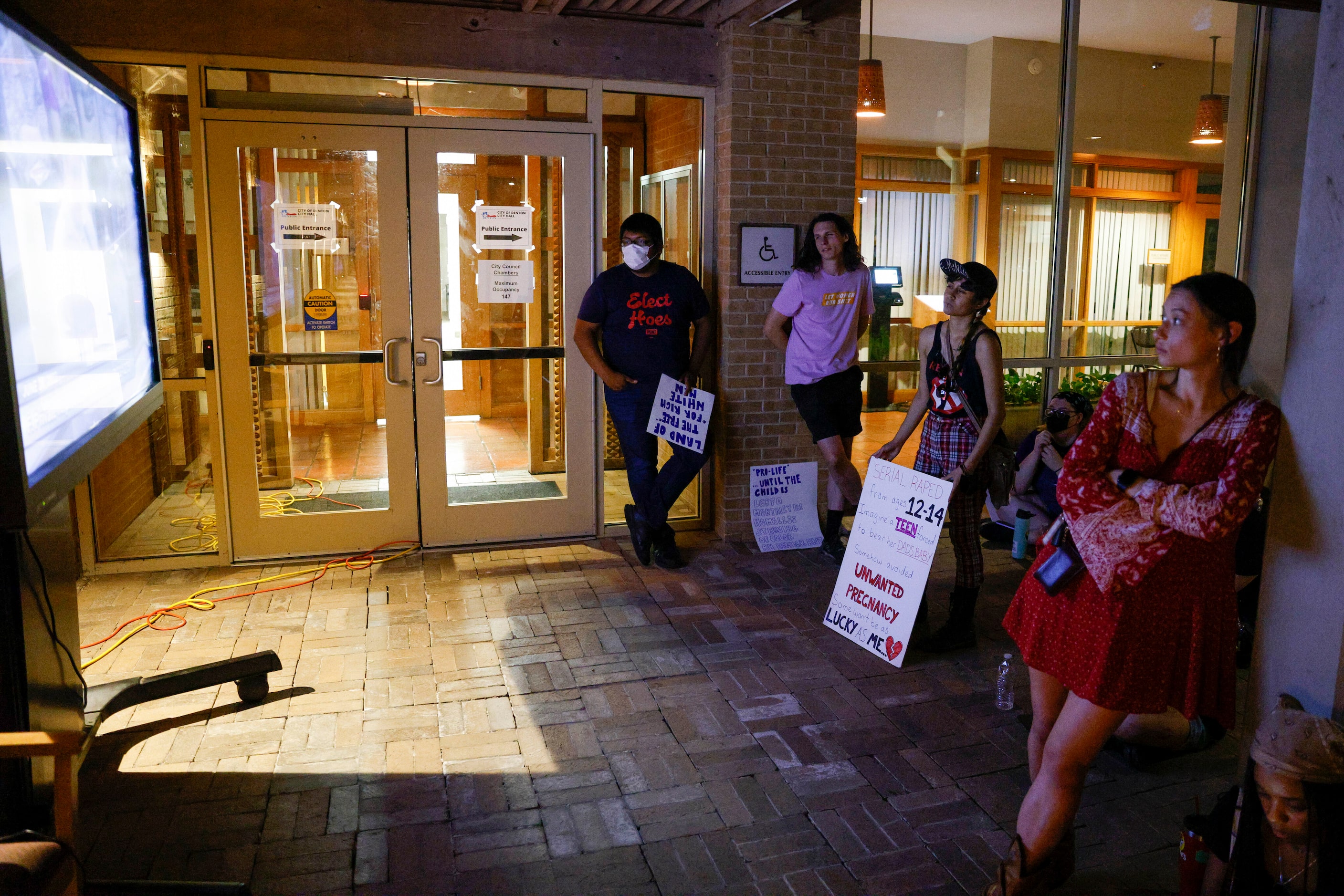 People watch a Denton City Council meeting on a tv outside Denton City Hall in Denton,...