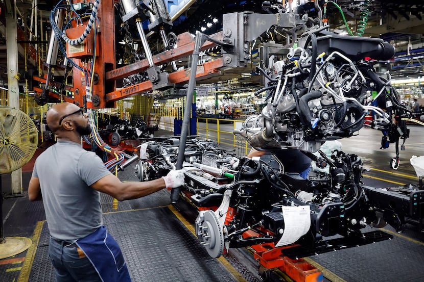 Assembly team worker Kevin Garner lowers the engine assembly onto the frame of a large SUV...