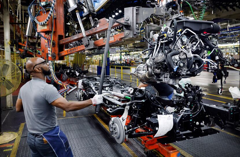 Assembly team worker Kevin Garner lowers an engine assembly onto the frame of a large SUV at...