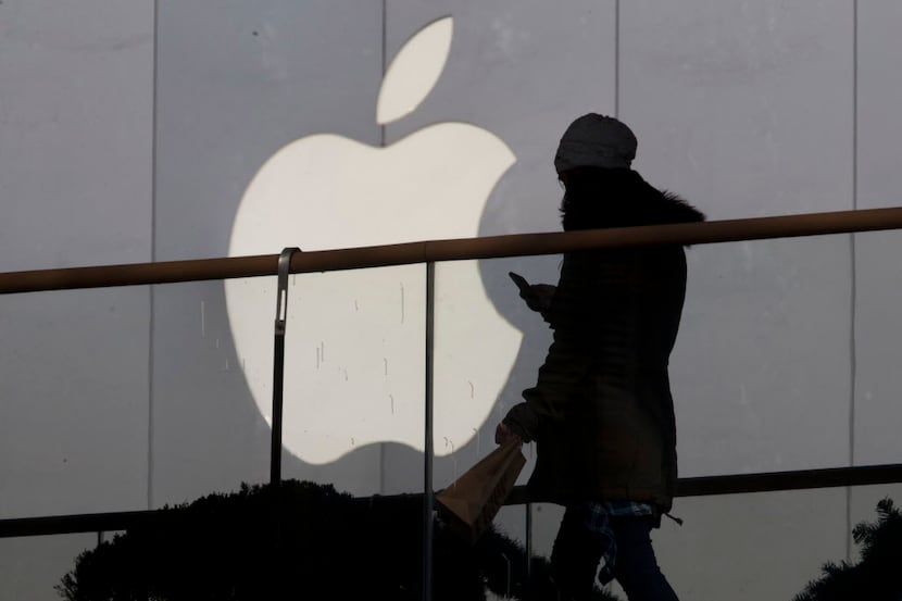 In this Dec. 23, 2013, file photo, a woman using a phone walks past Apple's logo near its...