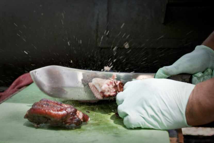 Fatty juices fly as Clyde Biggins uses a large knife to chop and separate smoked pork ribs...