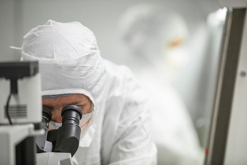 A BS&WH researcher wears a white hazmat suit while looking into a microscope.