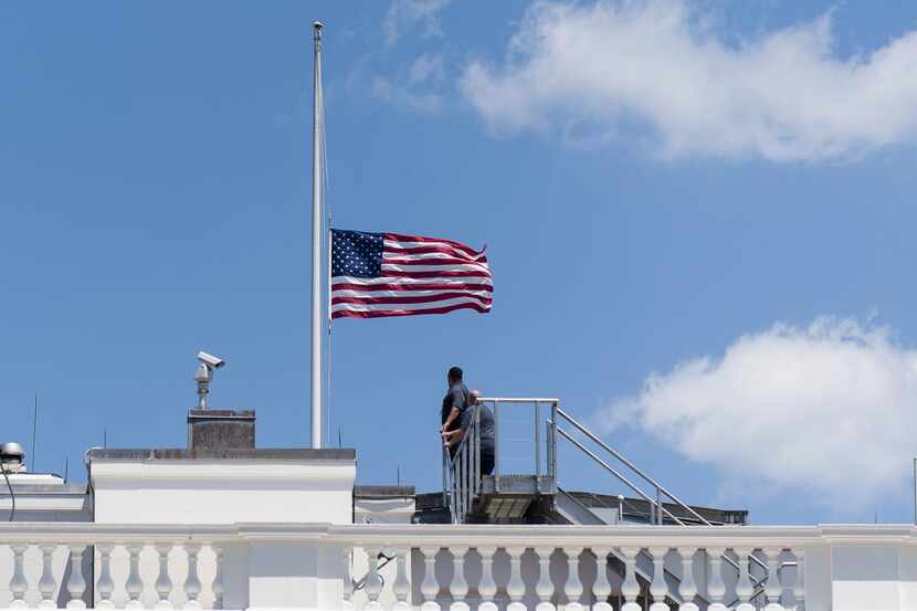 
White House personnel look back after lowering the flag on the roof of the White House to...