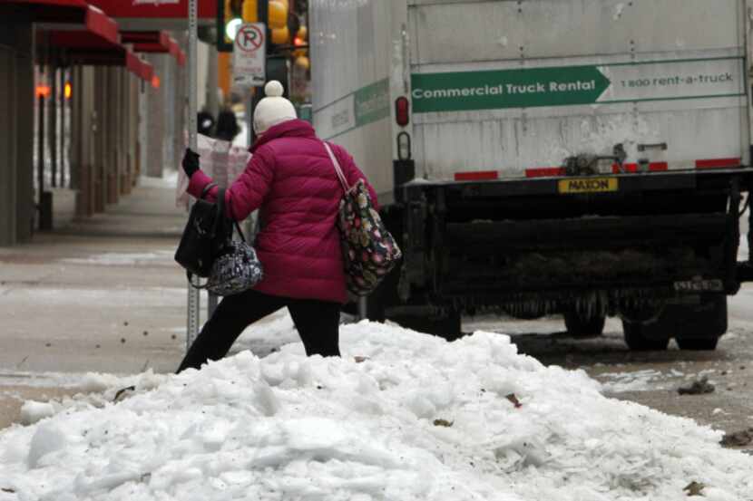 A pedestrian navigates her way through piles of snow and ice in downtown Dallas.