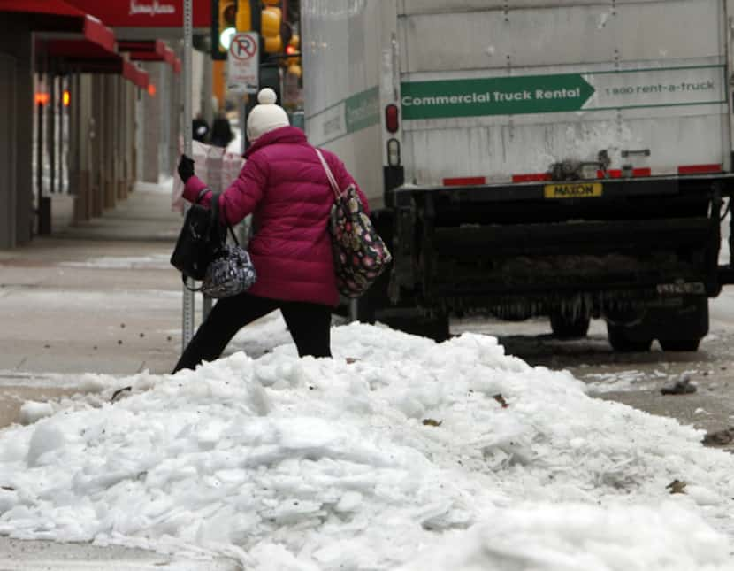 A pedestrian navigates her way through piles of snow and ice in downtown Dallas.