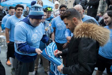 New York City FC forward David Villa, right, signs an autograph for a fan before helping...