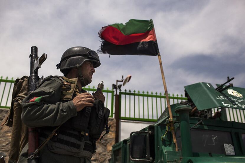 An Afghan policeman stands guard near an armored vehicle Thursday outside Cure International...