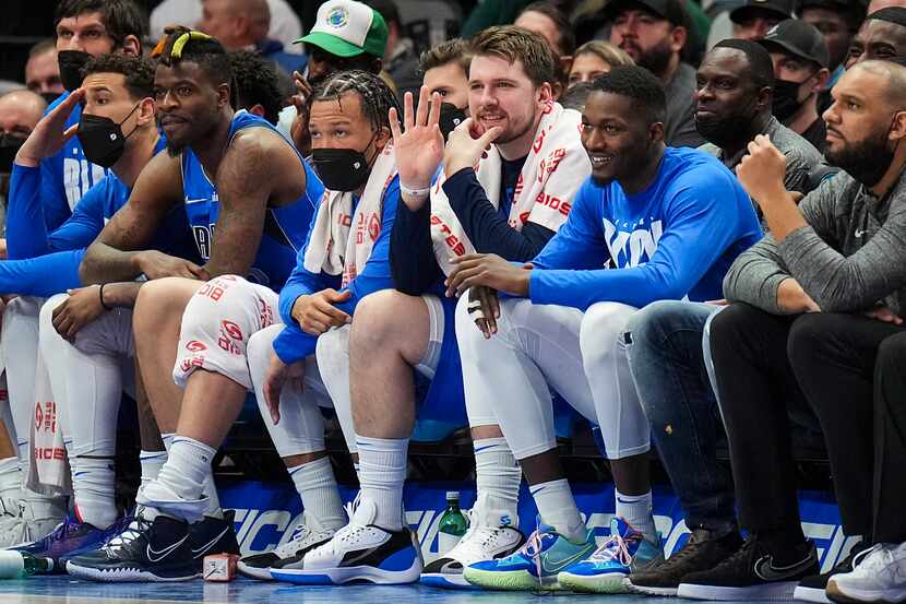 Dallas Mavericks guard Luka Doncic waves to teammates from the bench as he sits between...