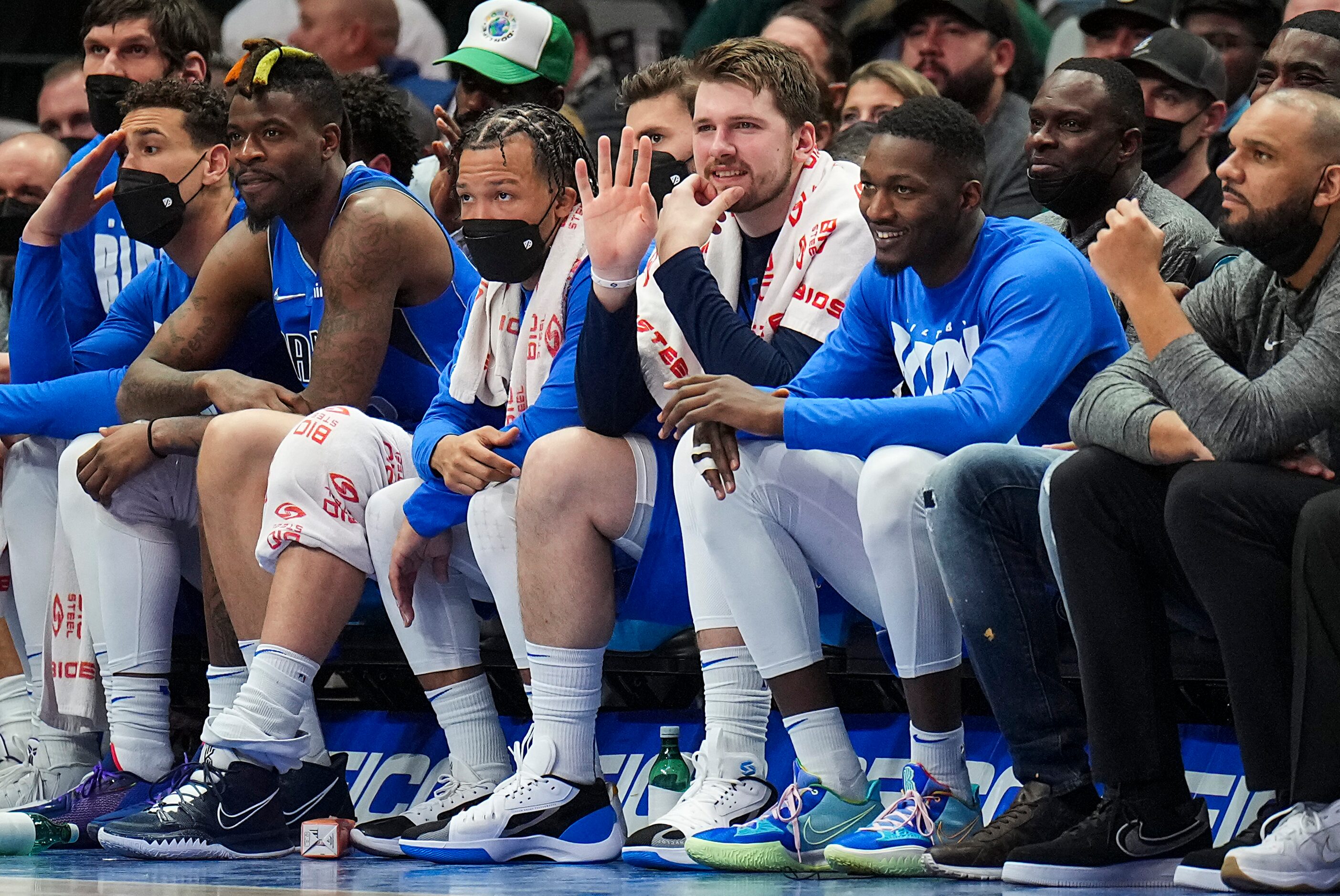 Dallas Mavericks guard Luka Doncic waves to teammates from the bench as he sits between...