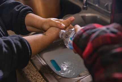 Rosa Mendoza washes her hands as David Sanroman, 7, pours water from a bottle after the...