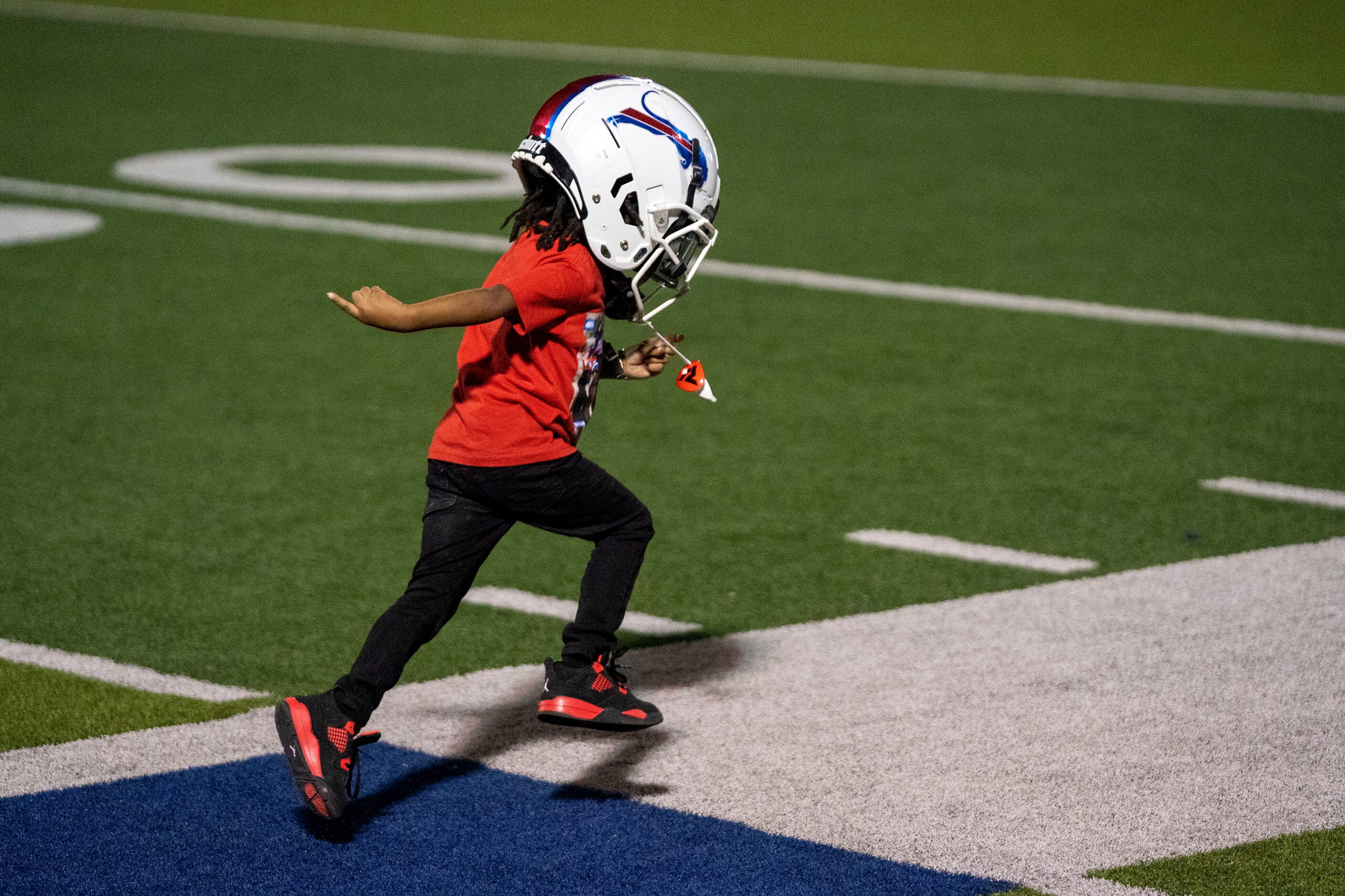 Ricko Demarcus-Williams, 3, runs down the sidelines while wearing the helmet of his older...