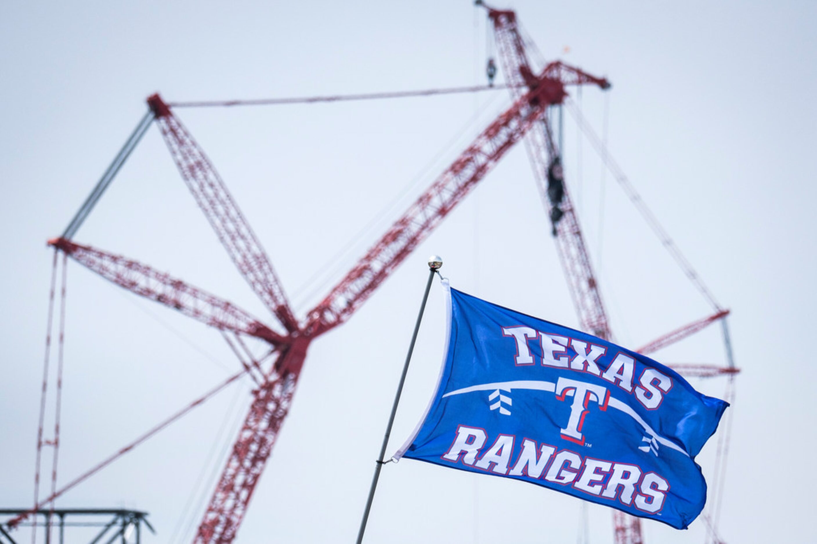 Cranes from the construction of Globe Life Field rises behind a Texas Rangers flag as fans...