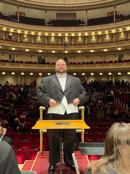 An orchestra conductor stands at the podium onstage at Carnegie Hall