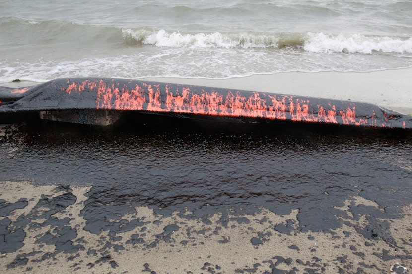 An oil containment boom sits in a puddle of oil Sunday on the beach along Galveston's...