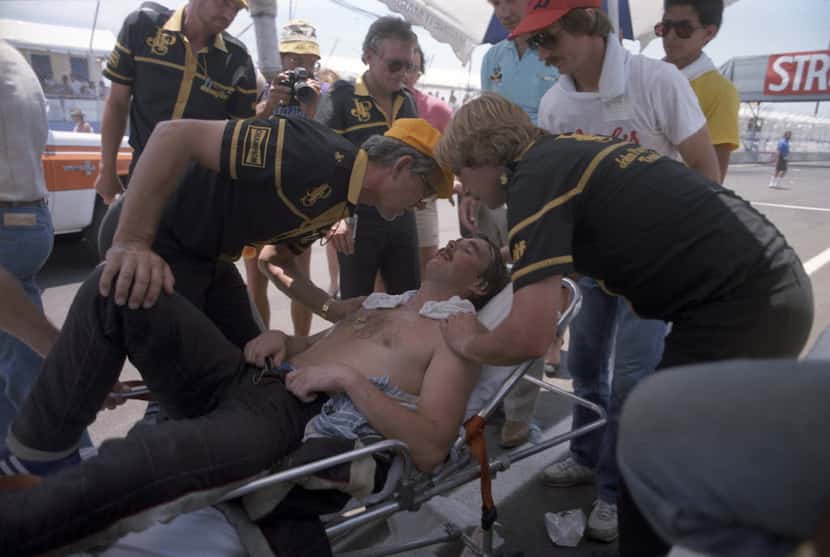 Driver Nigel Mansell is attended to after pushing his car at the end of the 1984 Formula One...
