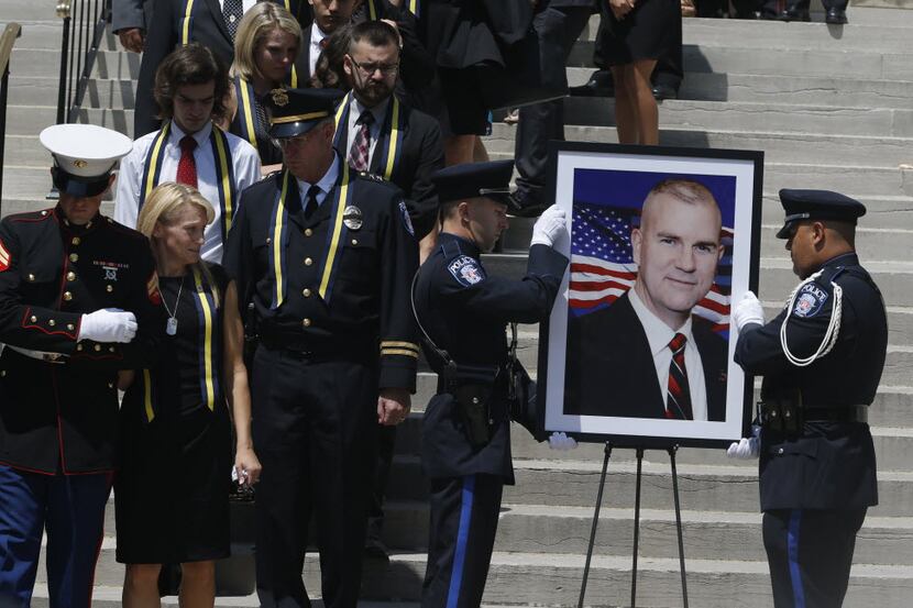 Tiffany McCullers (left) looks on as SMU police officers steady a portrait of her husband...