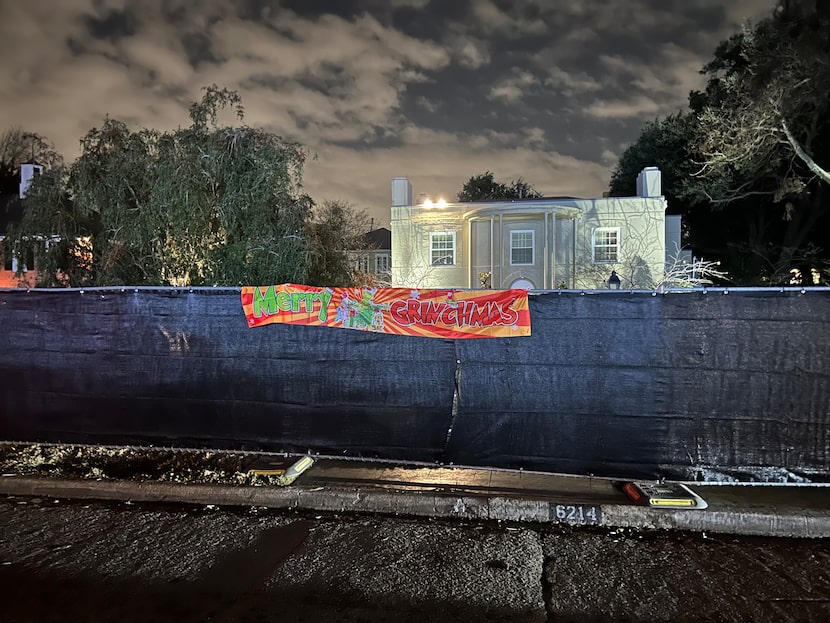 A banner with the words "Merry Grinchmas" on the fence opposite of the home.