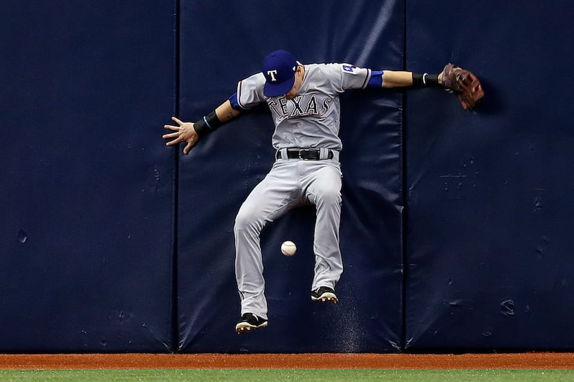 Texas Rangers center fielder Carlos Tocci crashes into the wall chasing a double by Tampa...