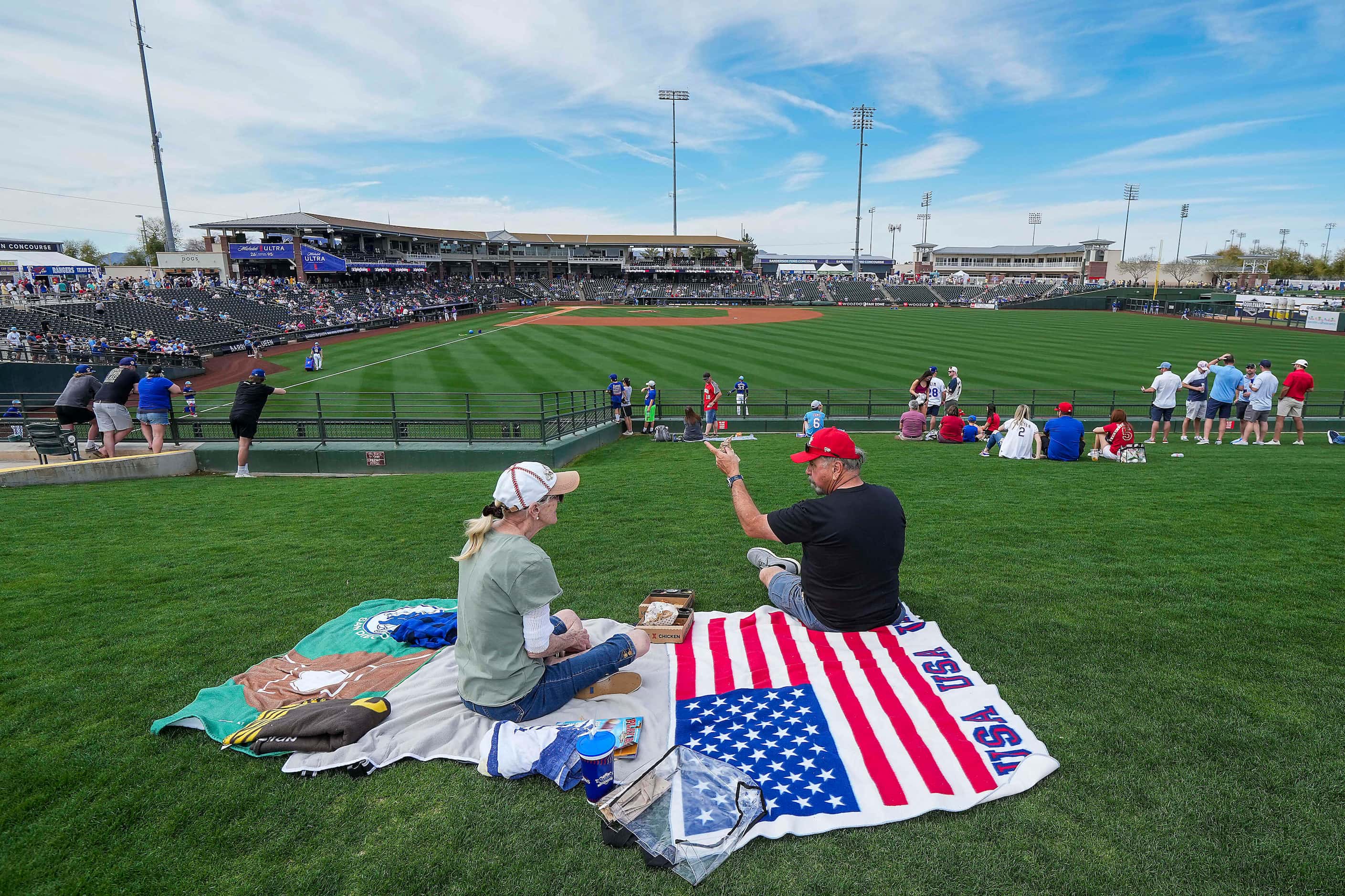 Fans settle in on the outfield berm before a spring training game between the Texas Rangers...