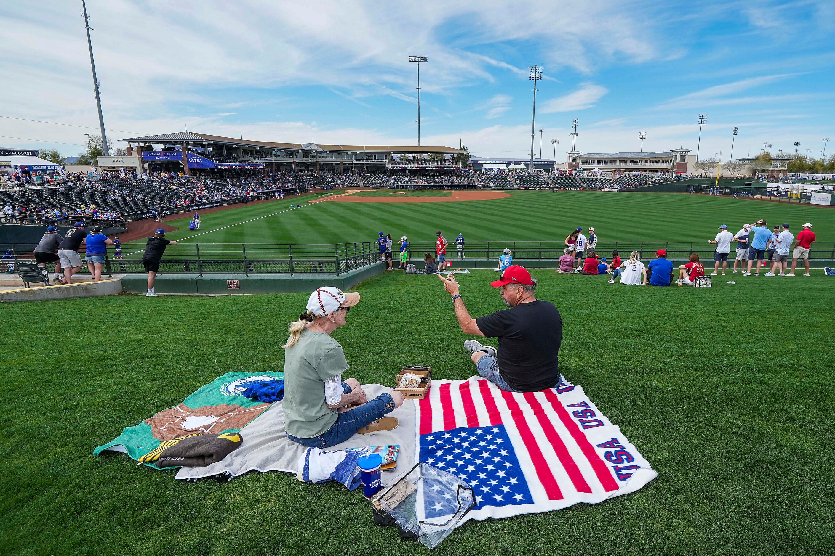 Fans settle in on the outfield berm before a spring training game between the Texas Rangers...