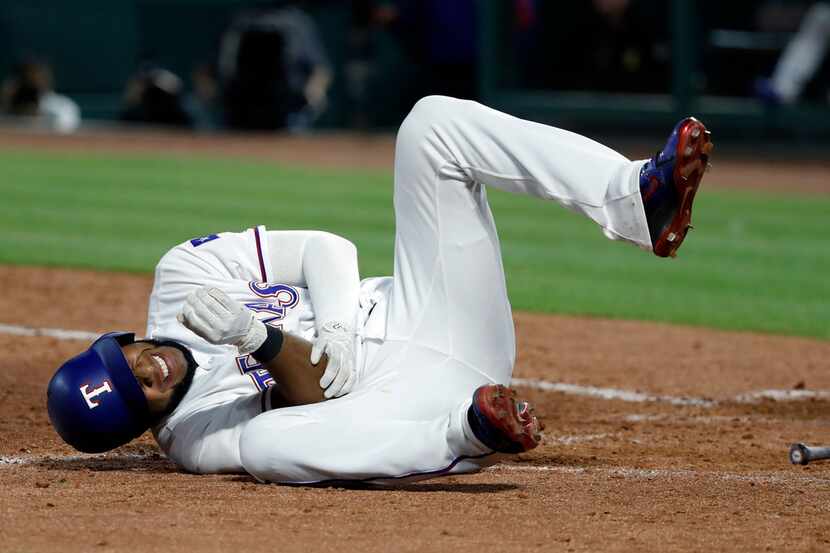Texas Rangers' Elvis Andrus rolls on the ground by home plate holding his right elbow after...
